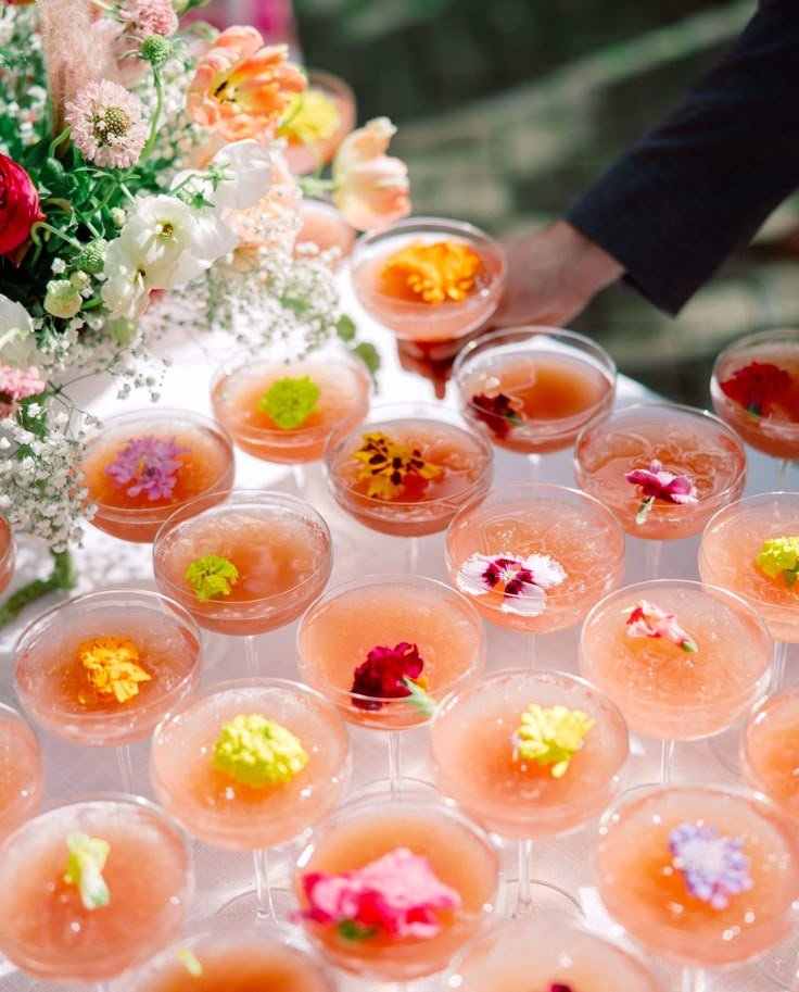 A tiered display of rose colored cocktails garnished with fresh edible flowers