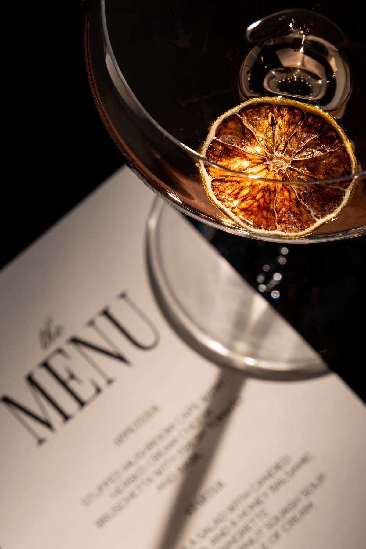 A dried citrus garnished cocktail resting on a printed drink menu at a Tonic and Timber event