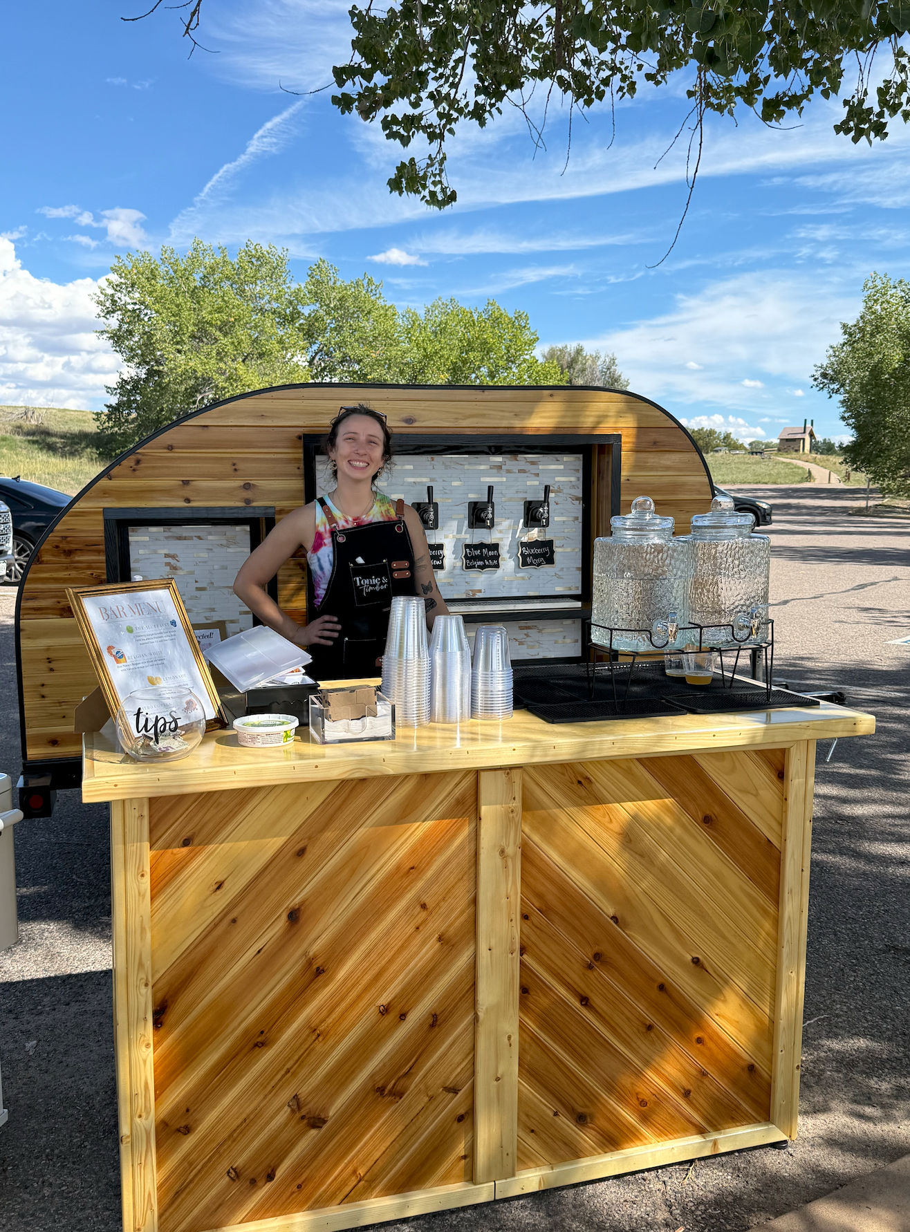 Kaley, owner of Tonic and Timber, smiling behind the tap trailer's beverage wall